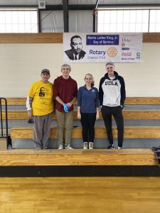 Sam Miglarese and Duke students, Brady Vaughan, Jessica Voss and Chase Frutos pose in front of a MLK Jr Day of Service Poster