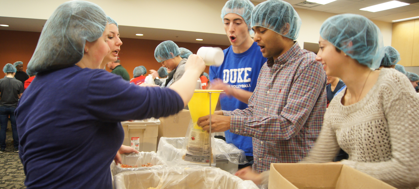 Duke student volunteers in hairnets package food during a million meals event