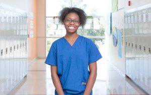 A young healthcare worker in blue scrubs poses in a hallway
