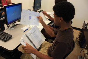 A middle school student reviews papers in front of a computer