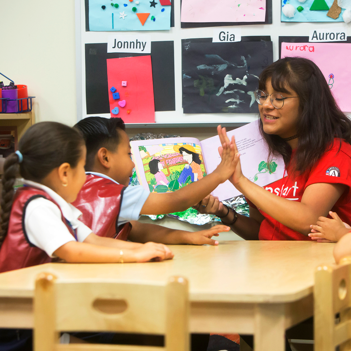 Jumpstart employee high fives a young child while reading to kids in a class